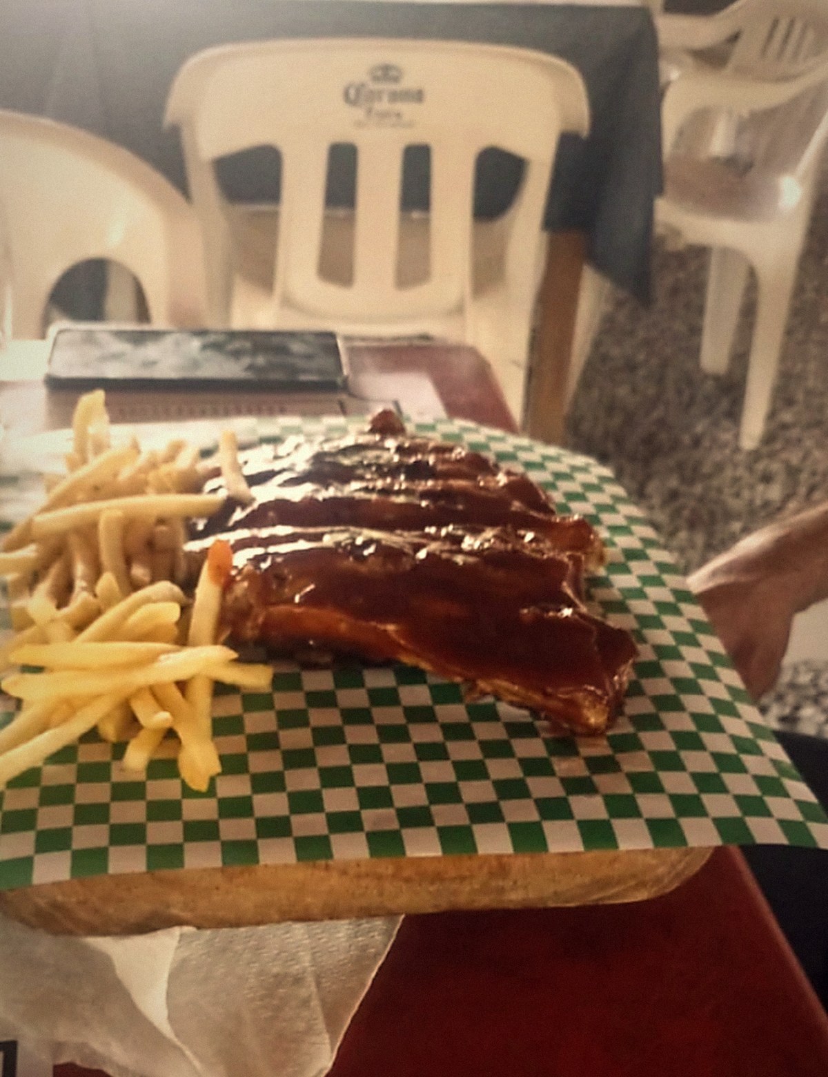 Costillas BBQ glaseadas sobre papel a cuadros verde con papas a la francesa
